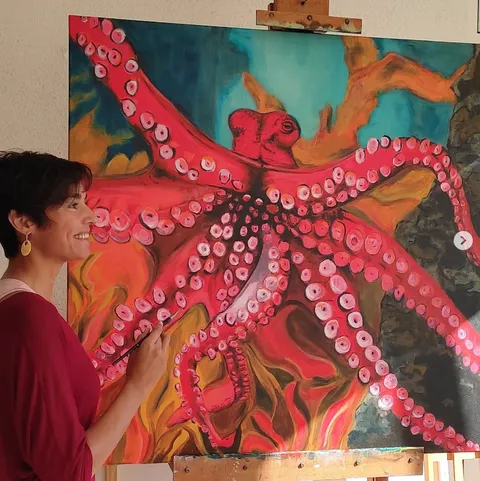 Una artista pintando un pulpo rojo sobre lienzo, expuesto en Dársena