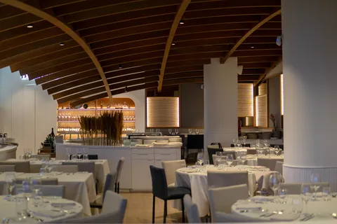 El comedor interior de Dársena, con el techo de madera, las mesas puestas y la cristalera al fondo