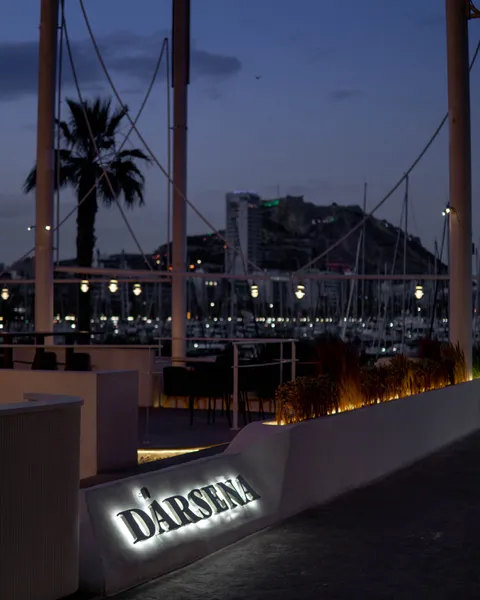 La terraza de Dársena de noche, con el rótulo iluminado y las luces del puerto y del castillo detrás